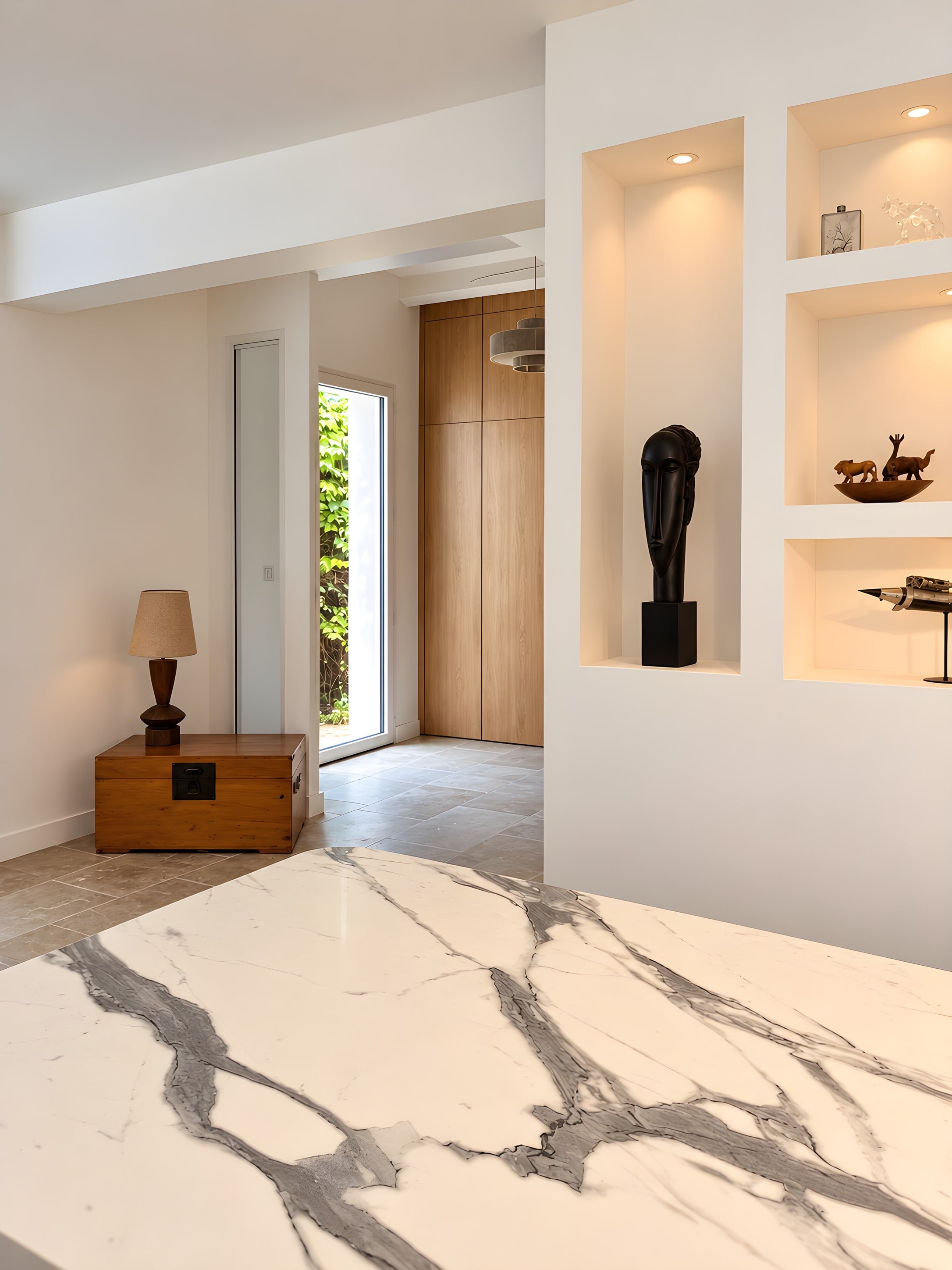 Niches en placo éclairées avec objets de décoration, placards en chêne dans l’entrée et plan en marbre au premier plan
